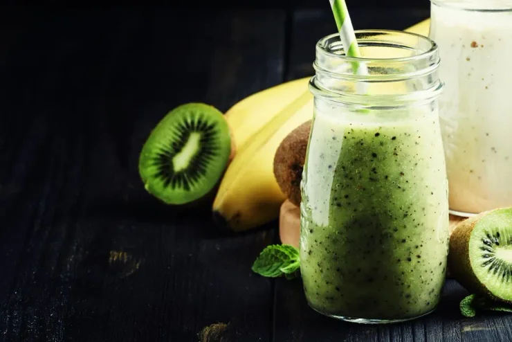 Morning Bliss Detox Smoothie in clear glass with straw. Banana and kiwi surrounding it