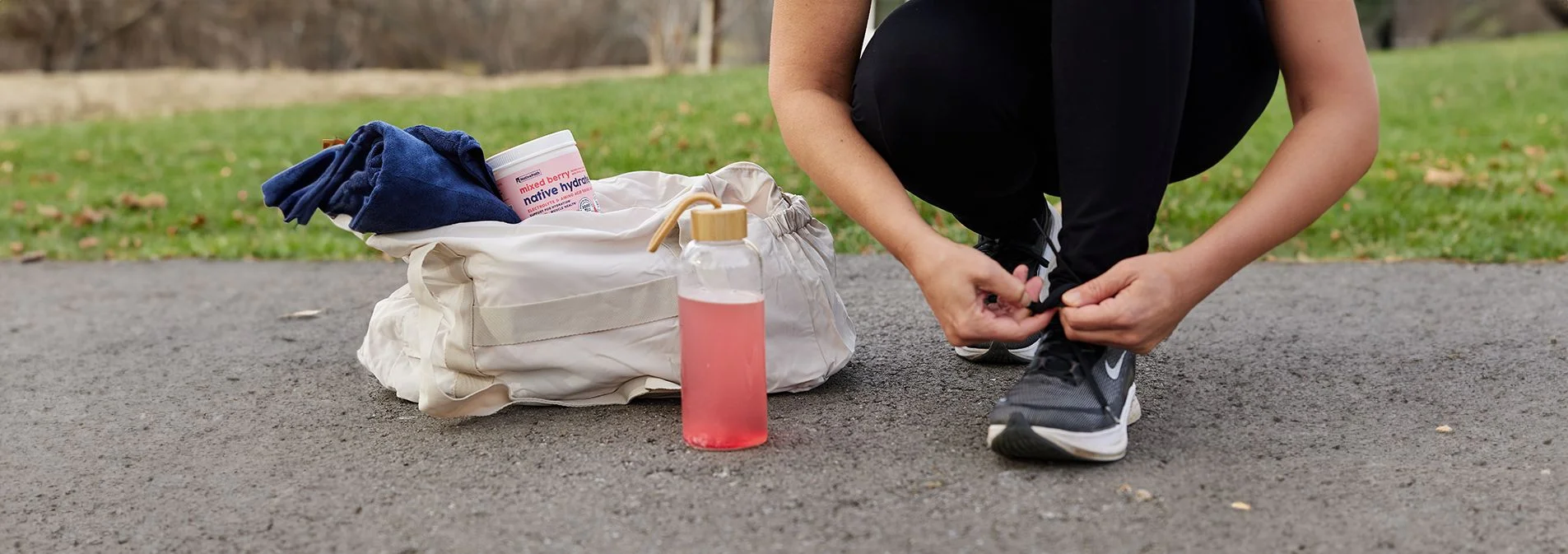 A woman tying her shoes with a container of Native Hydrate in her workout bag next to her