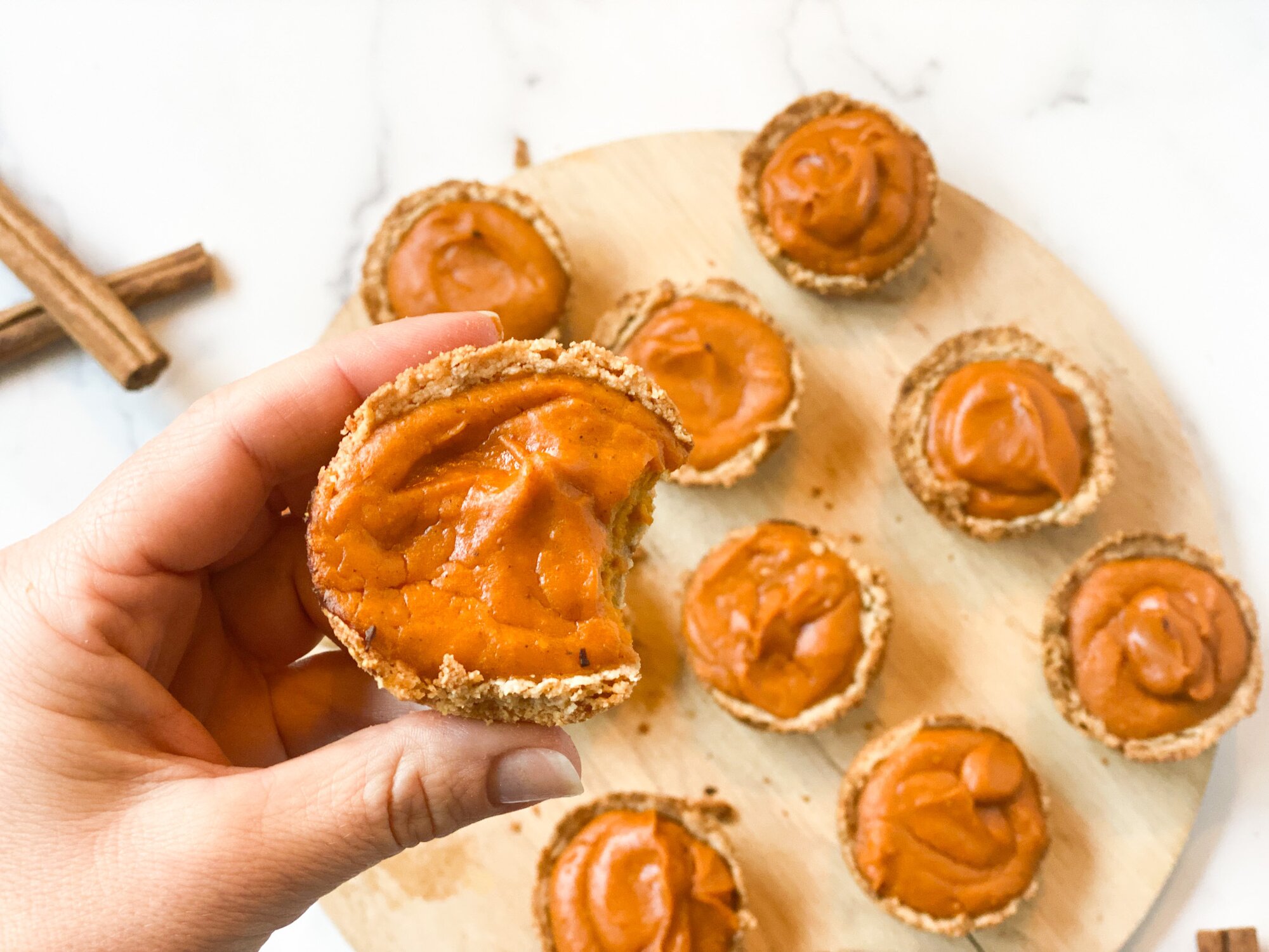 A hand holding a sweet potato tart with more tarts arranged on a wooden board in the background