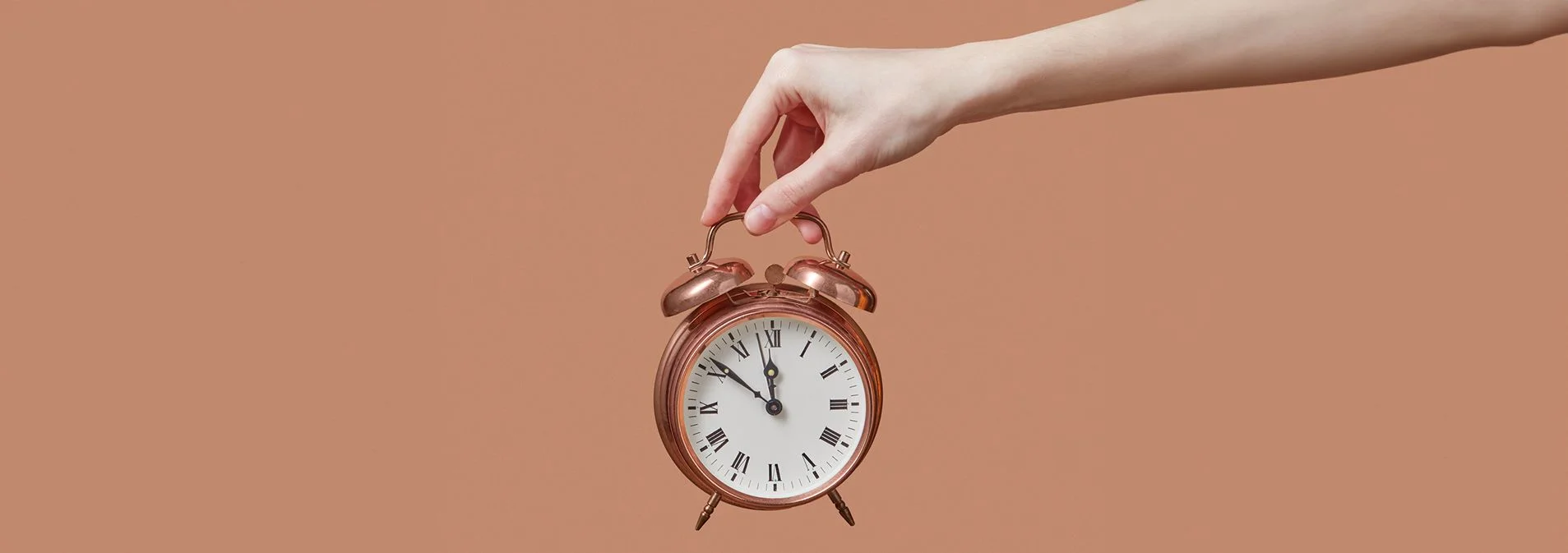 A hand holding a retro copper alarm with a salmon pink background
