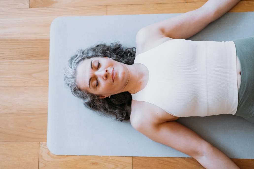 Overhead view of a woman with her eyes closed laying on a yoga mat