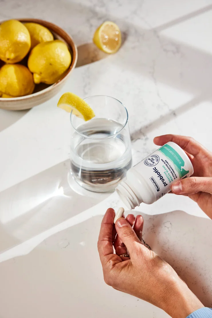 Female hand pouring a NativePath Probiotic capsule into her hand. Clear glass of water with a lemon slice in the background.