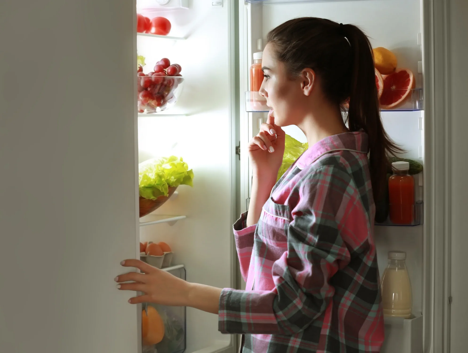 Young woman in pajamas looking into the fridge deciding what to eat for a night snack.