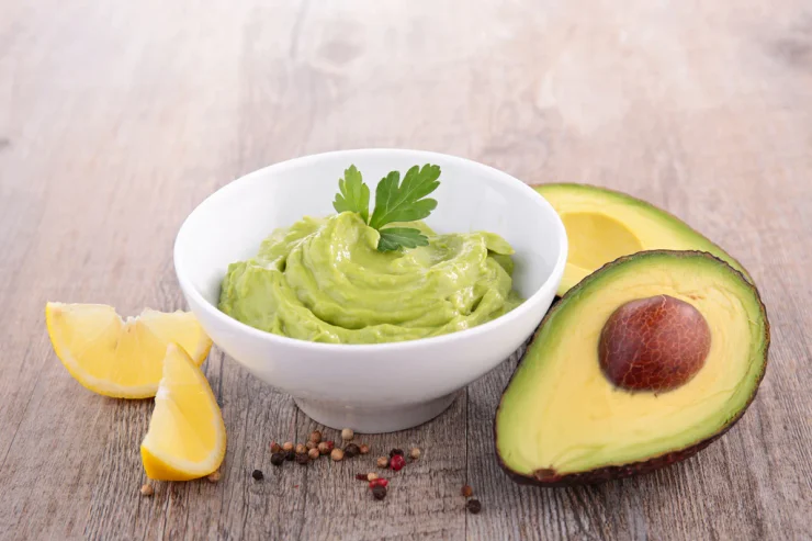 Two halves of an avocado next to a bowl of guacamole