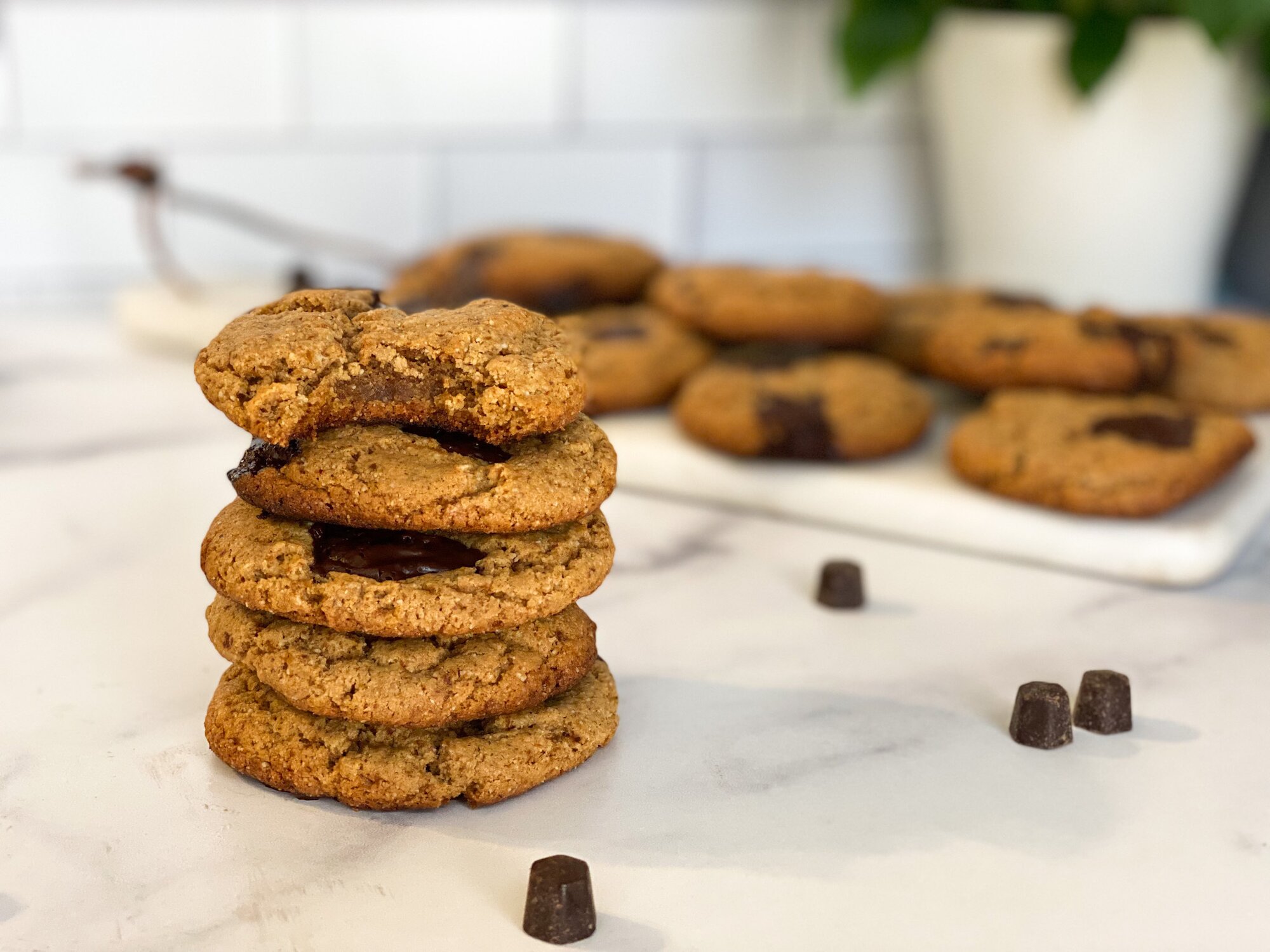 A stack of chocolate chip cookies sitting on a counter with more cookies in the background