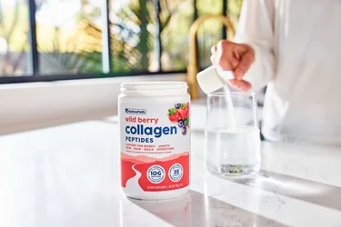 A hand pouring a scoop of NativePath Wild Berry collagen peptides into a glass of water