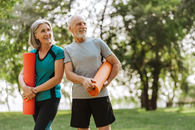 An older couple holding yoga mats outside and smiling.