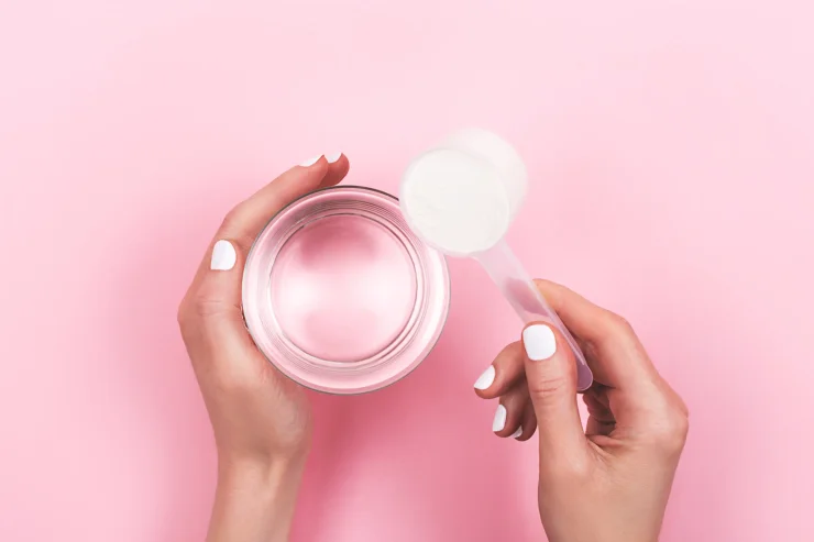 Woman hands with a scoop of collagen powder and a glass of water. Pro-aging supplement for healthy skin and bones. Flatlay, top view.