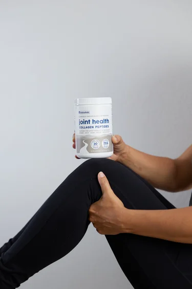 A woman with a container of NativePath Joint Health Collagen on her bent knee.