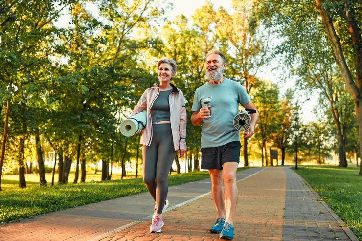 Older couple walking in the park with yoga mats