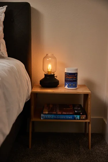 Frontal shot of a container of NativePath Collagen PM on a nightstand next to a lamp that is on.