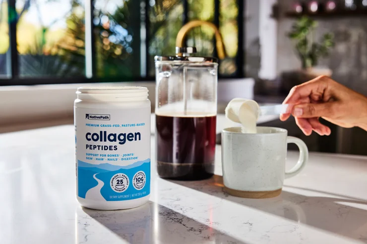 Hand stirring a scoop of NativePath Grass-Fed Collagen Powder into a cup of black coffee.