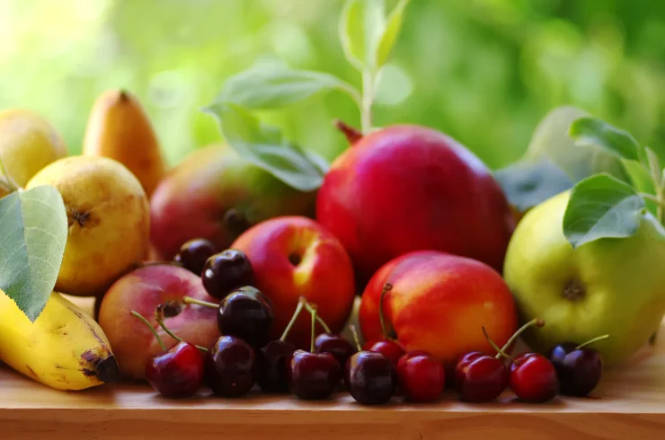 Assorted fruits on a wooden table: cherries, apples, and bananas.