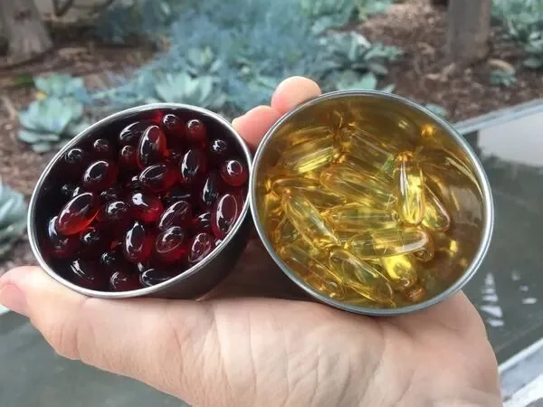 Hand holding krill oil capsules and fish oil capsules comparing the two.