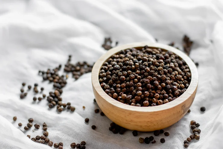 A large number of black peppercorns placed in a wooden bowl were placed on a white cloth.