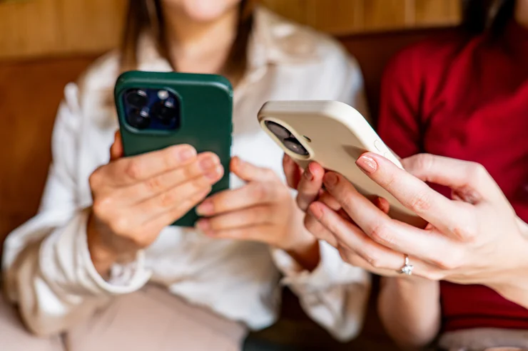 A close up of two women scrolling on cell phones 