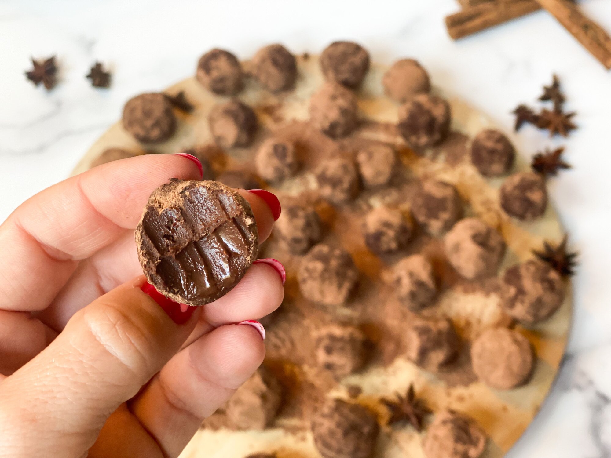 A hand holding a truffle with a bit taken out of it. More truffles in the background arranged on a wooden circular board.