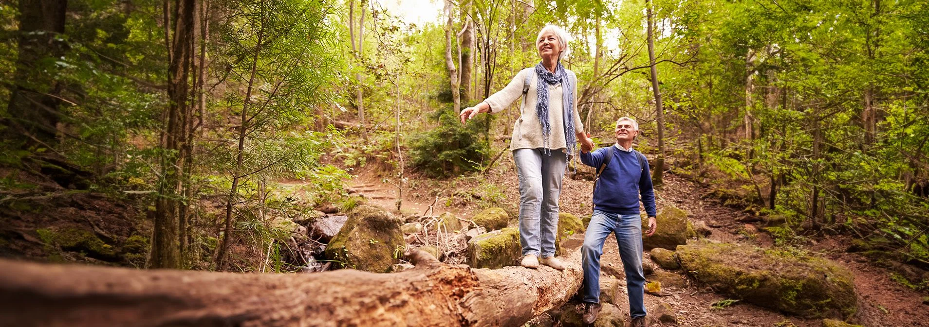 An older couple hiking, the woman is standing on a higher rock with the man holding her hand