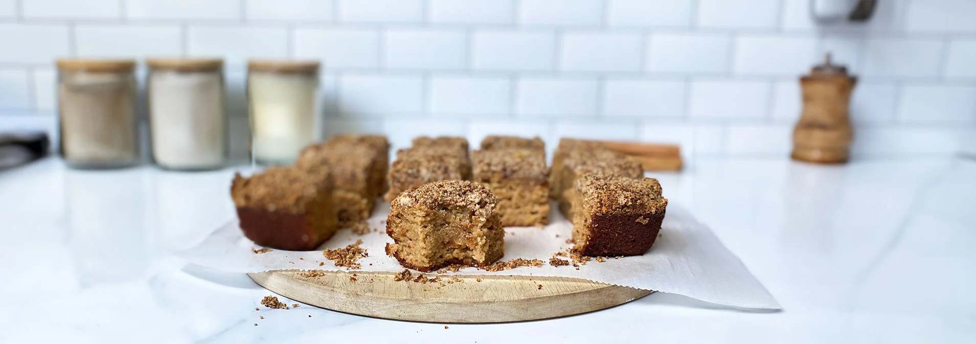 A close up shot of Spiced Paleo Crumb Cake on a circular wooden board. One piece has a bite taken out of it. 