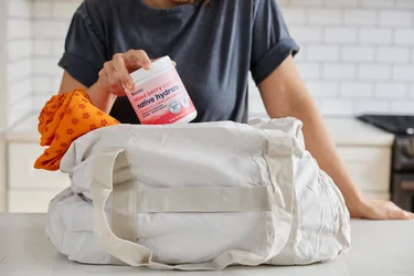 A woman putting a container of NativePath Native Hydrate Mixed Berry into a gym bag