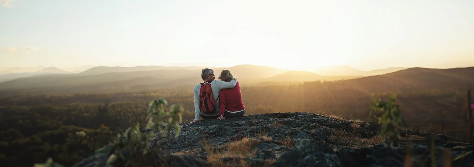 An active middle age couple sitting on a hiking trail watching a sunset together