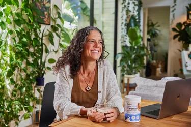 Adult woman sitting down at kitchen table enjoying cup of coffee with NativePath Coffee Creamer