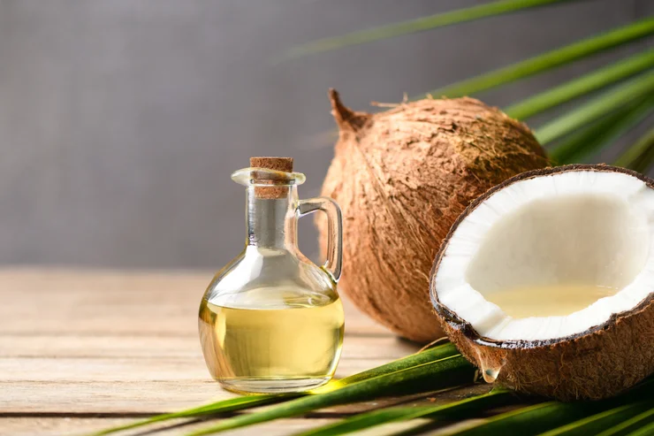 A glass jar of coconut oil with coconuts in the background