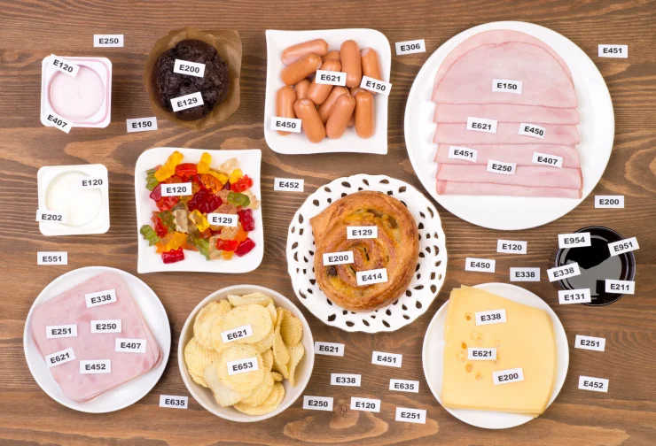 A variety of chemically perversaed foods like cookies and deli meat with labels of their chemicals