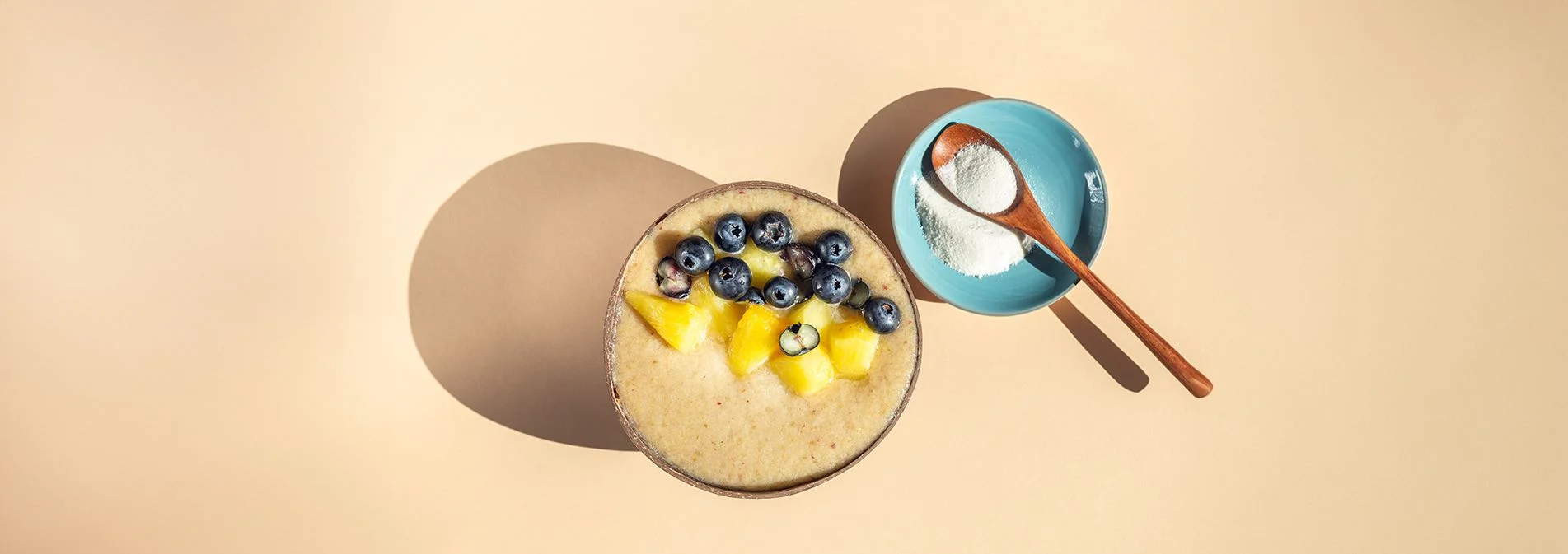 A spoon of collagen powder next to a smoothie bowl topped with fruit