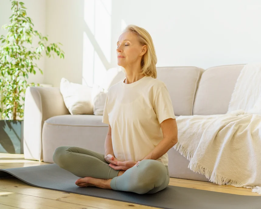 Older blonde woman sitting cross legged and closing her eyes doing a breathing exercise