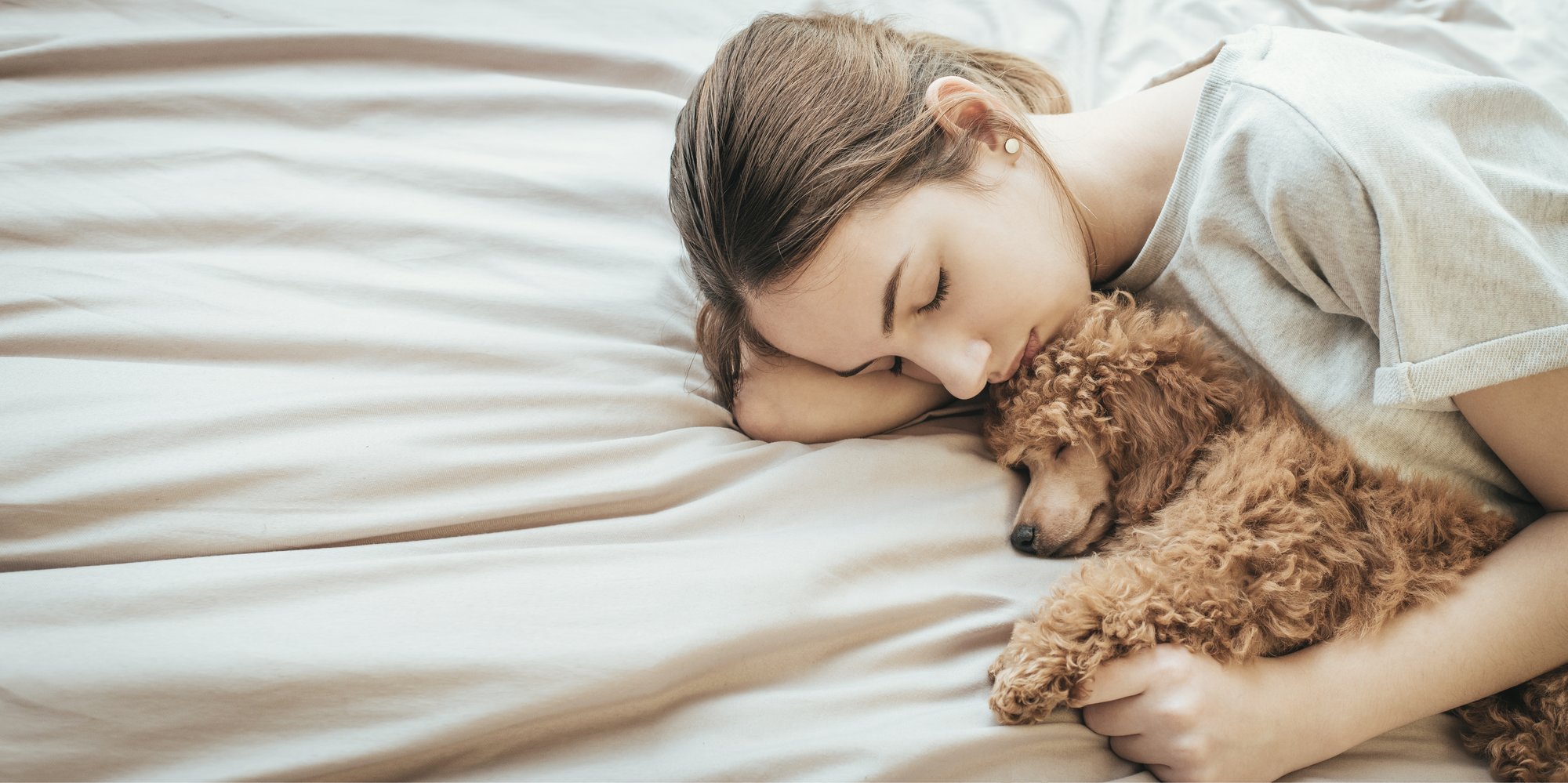 Woman sleeping in bed with a small golden poodle sleeping next to her