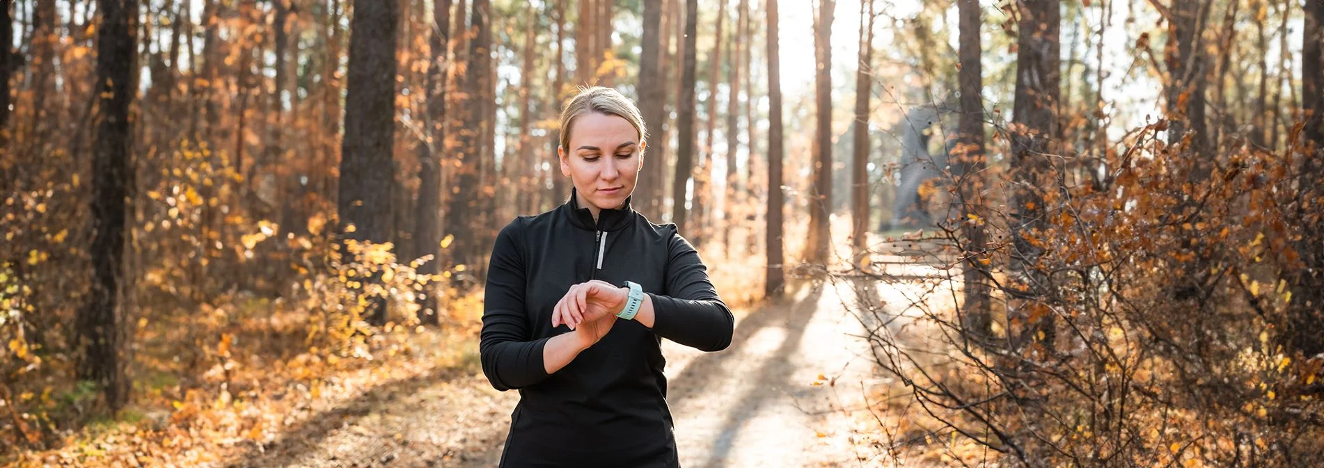 An older woman checking her heart rate on a watch while on a hike in the woods