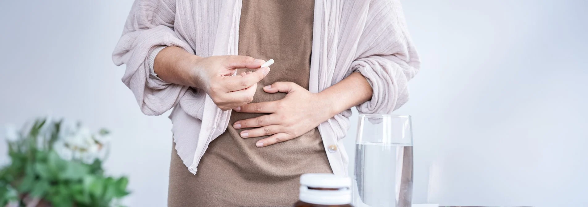 A woman holding her stomach and a probiotic pill in pain 