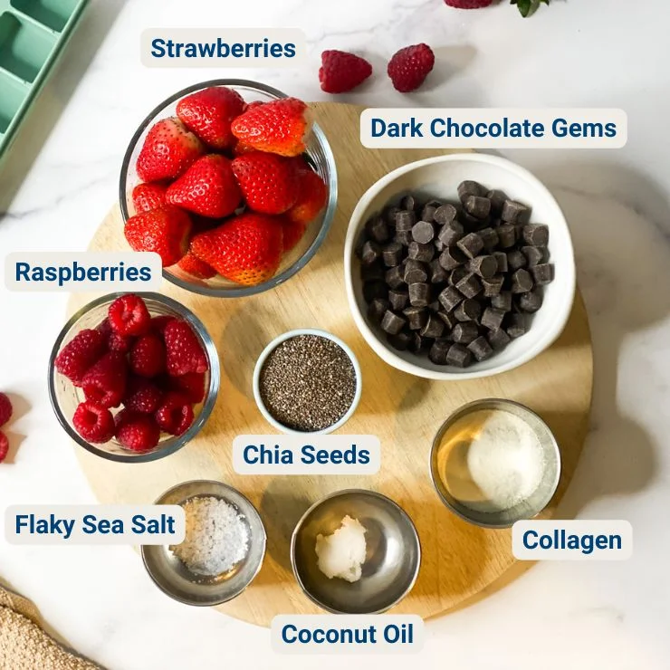Bowls of strawberries, raspberries, dark chocolate, chia seeds, collagen, coconut oil, and sea salt