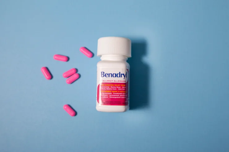Benadryl Allergy Medication with Pink Pills Scattered on Light Blue Background