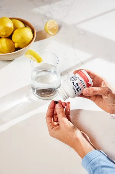 A hand p holding a bottle and softgel of NativePath Antarctic Krill Oil with a glass of water in the background