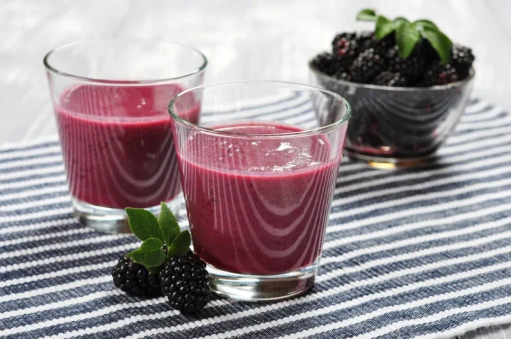 Two clear glasses of Collagen Berry Detox Smoothie with a bowl of blackberries in the background