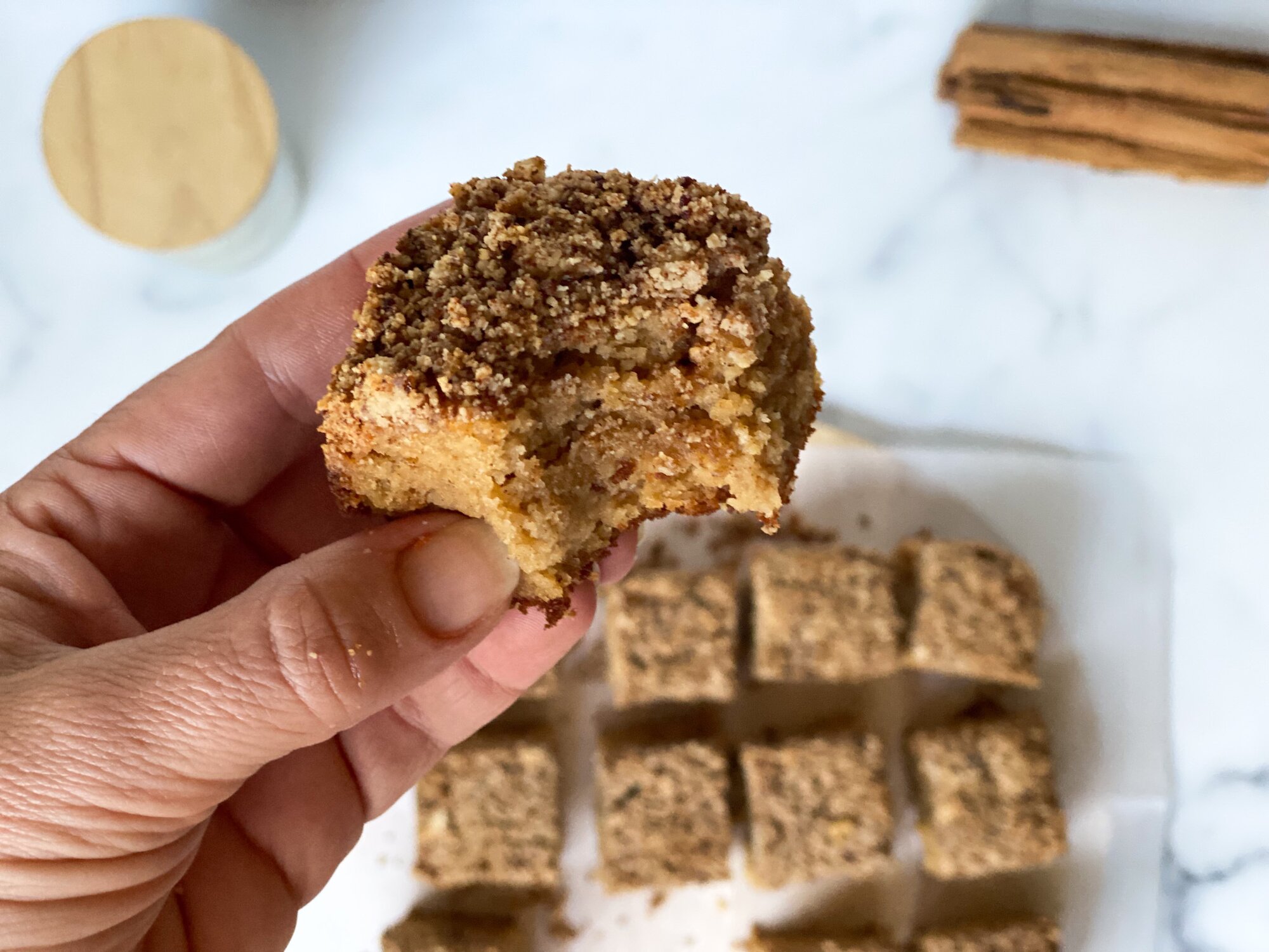 A close up of a hand holding a piece of Spiced Paleo Crumb Cake with a bite taken out of it.