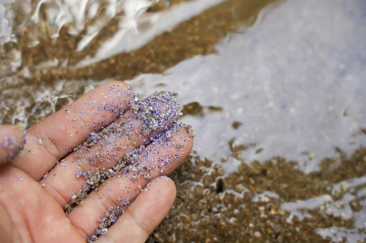 Microplastics on a hand with sand and ocean water in the background