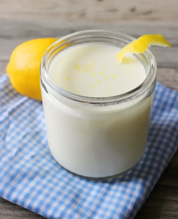 Clear glass of Lemon Olive Oil Drink with lemon zest sprinkled on top. Whole lemon in background