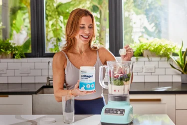 A woman pouring a scoop of NativePath Collagen peptides into a blender full of fruits and veggies
