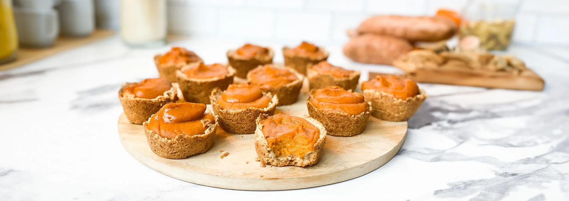 Front view of sweet potato tarts arranged on a circular wooden board. A bite is taken out of one tart.