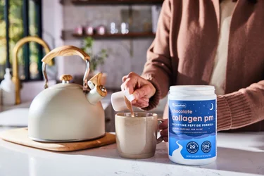 A woman pouring a scoop of NativePath Chocolate Collagen PM into a mug
