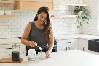 A woman pouring a scoop of NativePath Joint Health Collagen into a coffee mug.
