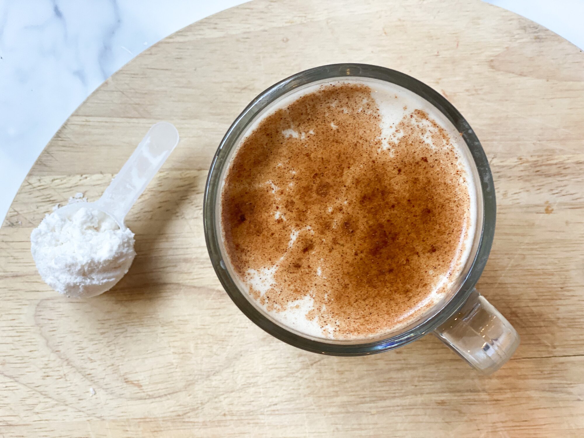 A top view of the MCT Collagen Latte in a glass mug with a scooper of NativePath MCT Powder next to it.