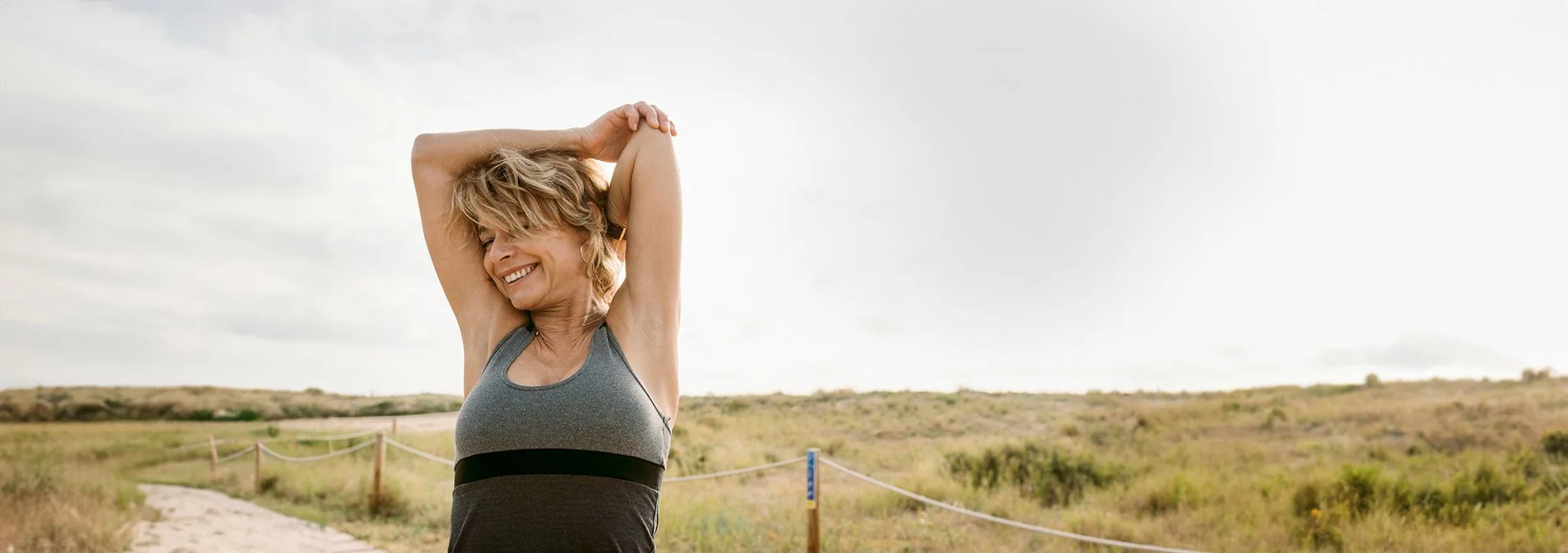 A woman outdoors walking on a trail stretching