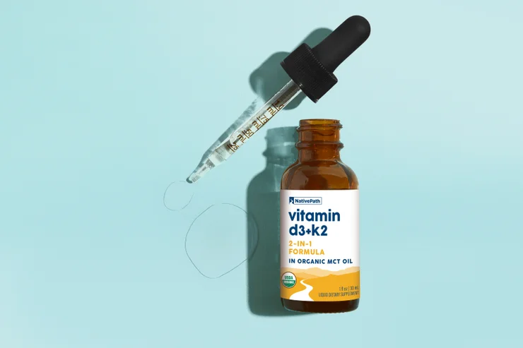Hand squeezing Vitamin D3 + K2 dropper against light blue background