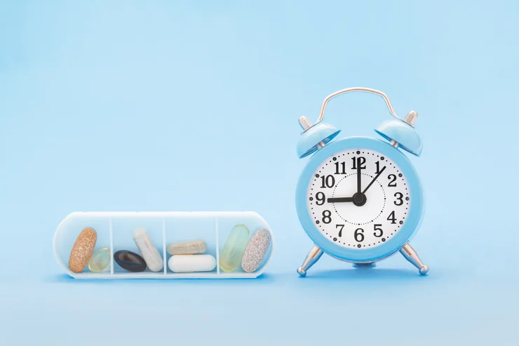 An alarm clock with a pill box next to it on a blue background