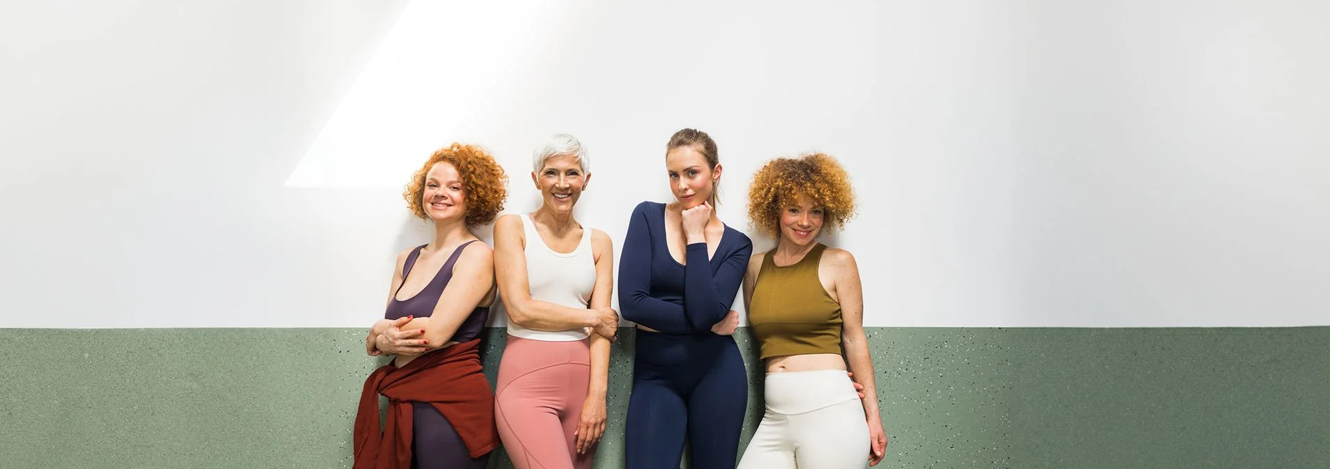 A group of 4 women leaning against a white and green wall