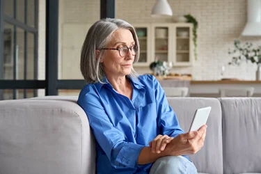 An older woman looking at her smartphone while sitting on a couch